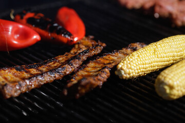 Corn, red paprika and pork ribs on an outside charcoal metal grill