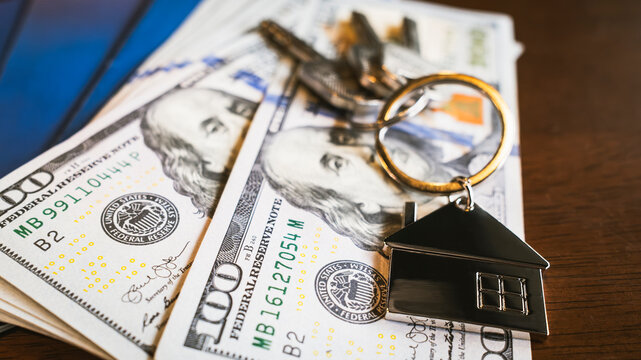 Real estate finance concept with house keychain and keys placed on money bills. Symbol of home purchase, property investment, mortgage loan, housing finance, financial planning, and ownership cost.