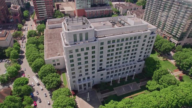 Descending aerial above the granite and marble Federal Reserve building in midtown Atlanta, surrounded by a lush tree canopy with the modern city skyline behind on a bright summer day.
