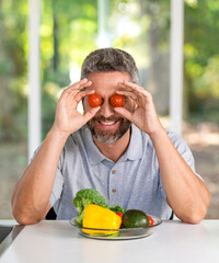 Man having fun with vegetable in kitchen. Mature man eating lunch. Having funny lunch in kitchen....