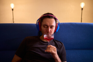 Relaxed man enjoying wine, Person wearing headphones rests peacefully, Creative professional enjoys evening relaxation with wine and soothing music in modern living space © Евгений Вершинин
