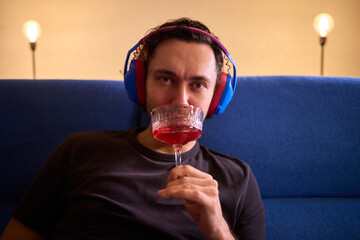 Relaxed man enjoying wine, Person wearing headphones rests peacefully, Creative professional enjoys evening relaxation with wine and soothing music in modern living space © Евгений Вершинин