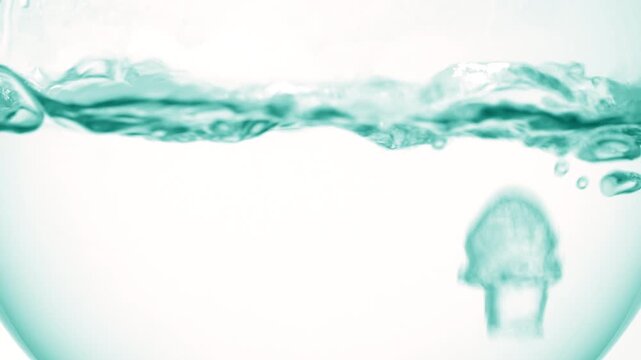 Immense hyper-close view of luminous clear liquid boiling in a round-bottom flask, producing bubbles and waves over soft gray background | Urea solution cosmetic science concept