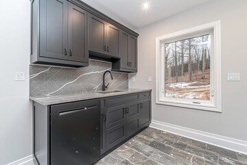 A modern kitchen with dark cabinetry and a stone backsplash, featuring a large window that offers a view of a wooded area outside.
