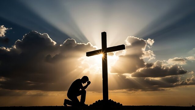The silhouette of a man kneeling in humble prayer at the foot of a wooden cross with bright sun rays breaking through dramatic clouds.