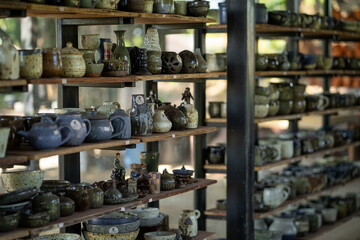 Handcrafted pottery displayed on wooden shelves, showcasing various shapes and colors. collection includes mugs, bowls, and decorative items, creating warm and inviting atmosphere
