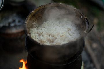 Steaming rice in bamboo basket over fire, creating warm and inviting atmosphere. steam rises, enhancing aroma of freshly cooked rice