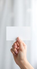 Female hand holds up blank white rectangular card against a pale, bright background
