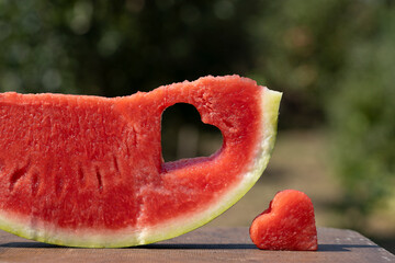 Fresh juicy red watermelon slice with heart shape hole on nature background in outdoors garden in summer time, closeup. Concept of happiness, love, holidays and vacation