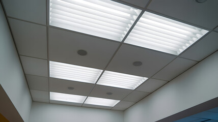 Close up view of a modern suspended grid ceiling with square white louvered light panels providing bright even illumination in a clinic or office space..png