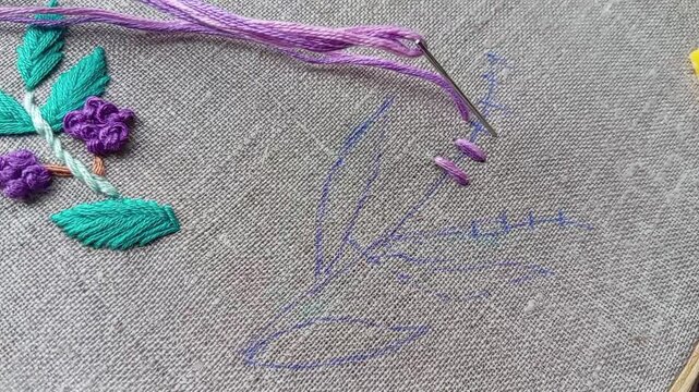 Close-up tutorial video of a hand embroidering a purple flower using hand stitch technique, part 2. Educational needlework content showing floral embroidery step by step for DIY learning.