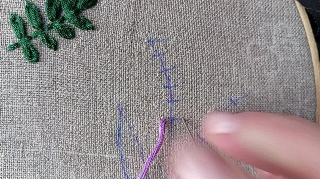 Close-up tutorial video of a hand embroidering a purple flower using hand stitch technique, part 1. Educational needlework content showing floral embroidery step by step for DIY learning and craft 