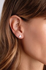 Close-up of a woman's ear with small, triangle-shaped earrings
