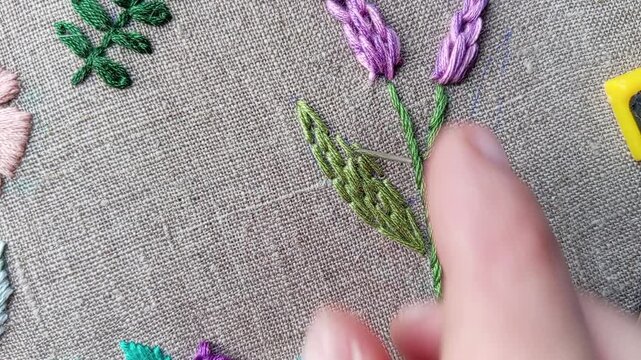 Close-up tutorial video of a hand embroidering a green leaf for a purple flower using satin stitch technique. Educational needlework content showing smooth leaf filling step by step for embroidery lea