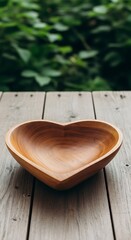 Heart shaped wooden bowl rests upon weathered wooden planks with foliage background