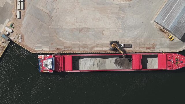Direct overhead drone of cargo ship aligned along port quay in industrial harbor