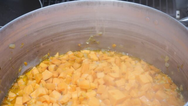 An extreme close-up serves as a process-oriented insert shot, capturing the initial saut&eacute;ing phase of a traditional West African soup.