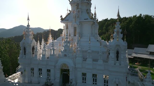 Aerial drone footage of the Loha Prasat Sri Mueang Pong pagoda temple in Chiang Mai, Thailand, on a sunny day, showcasing traditional architecture surrounded by nature.