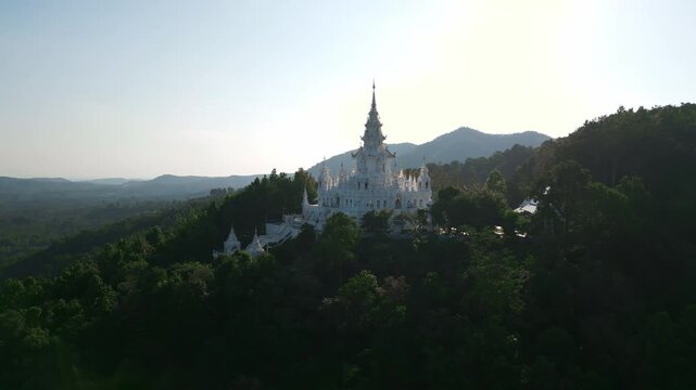 Aerial drone footage of the Loha Prasat Sri Mueang Pong pagoda temple in Chiang Mai, Thailand, on a sunny day, showcasing traditional architecture surrounded by nature.