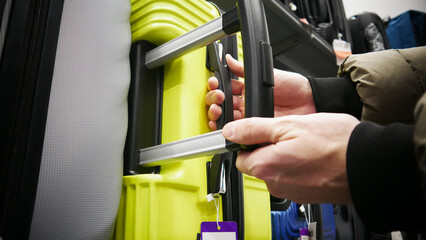 Close-up of a male buyer's hands choosing a plastic suitcase in a shopping mall