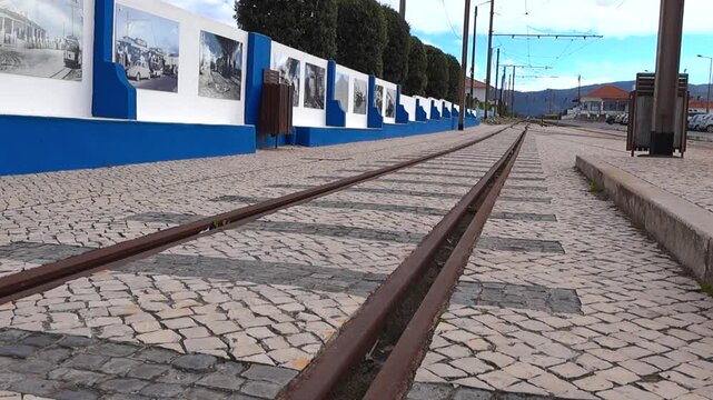 Low-angle cinematic glide along the rusty Sintra tram tracks set into traditional calcada portuguesa cobblestone pavement at Azenhas do Mar on a cloudy day with no people.