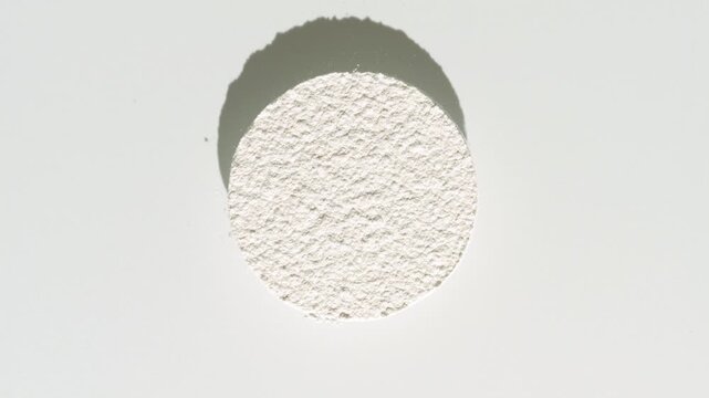 Overhead shot of white powder sifted in form of circle projects a moving shadow on a dim grey background