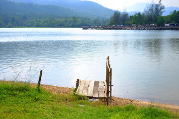 Rustic wooden bridge on riverbank with thatched building by the river for customers to dine and tropical forest background