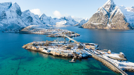 Aerial view of Sakrisøy in the Lofoten Islands, where bright yellow rorbuer fishing cabins stand out against snowy winter landscapes and striking turquoise-blue Arctic waters. © Remo Peer