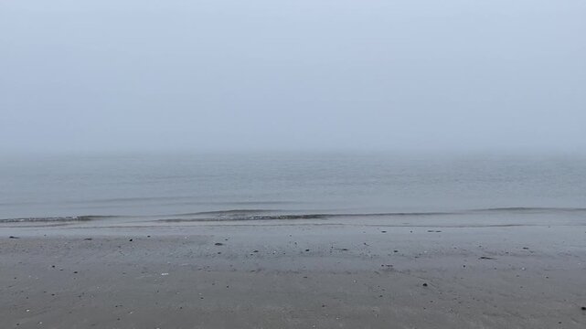 A desolate grey beach with rippled sand stretching towards the misty adriatic sea under a hazy foggy sky. Cervia. Italy