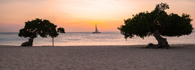 Witness the tranquil sunset casting vibrant hues over Eagle Beach in Aruba. Sailboats drift in the...