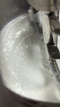 Macro close-up of a stainless steel mixing tank where an agitator blends a thick white emulsion. Ideal for concepts of skincare manufacturing, cosmetic formulation, quality processing, and industrial.