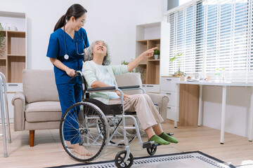 Fototapeta premium Smiling physiotherapist taking care of the happy senior patient in wheelchair at home.