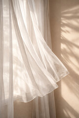 White sheer curtains gently blowing in sunlight with soft leaf shadows on a beige wall.