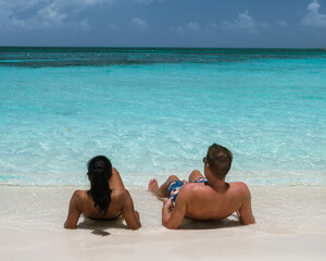 Two people enjoy a tranquil moment on Palm Beach in Aruba, soaking in the sun and the stunning...