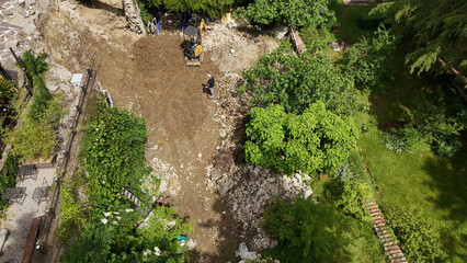 Construction worker operating mini excavator during earthmoving works in a garden, transforming the landscape with heavy machinery and manual labor © Antonia
