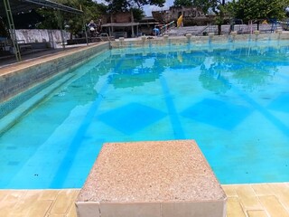Starting block at the edge of a public swimming pool with clear blue water. Aquatic facility for professional training, sports competition, and healthy lifestyle concepts.