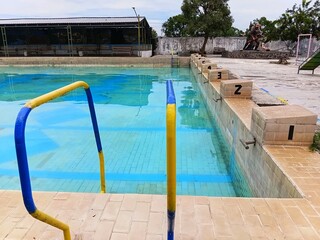 Yellow and blue metal handrails at the edge of a public swimming pool. Close-up of pool entry with clear water and tan tiles, ideal for summer recreation and safety concepts.
