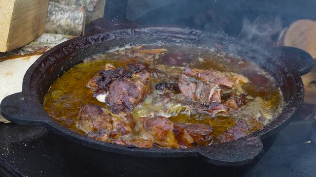 Roast in a cauldron. Boiling, fatty broth with meat is fried and simmered on an outdoor stove, close-up footage.