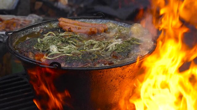 Roast in a cauldron. Boiling, fatty broth with meat is fried and simmered on an outdoor stove, close-up footage.