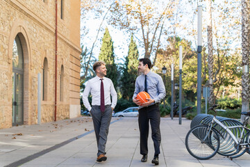 Fototapeta premium Two business colleagues in formal attire walking outdoors having a conversation with basketball