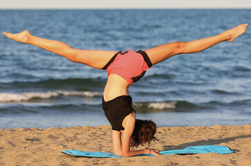 teenage girl with her head down does gymnastics by sea
