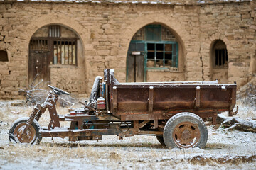 Weathered three-wheeled cargo vehicle abandoned in courtyard of historic village building