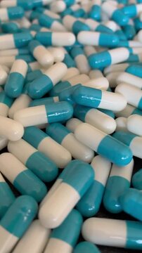 Vertical view blue and white capsules rotating on black surface for pharmaceutical and healthcare supply.