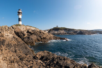 lighthouse standing on a rocky cliff by the deep blue sea under a clear sky, Isla de Pancha, Ribadeo, Galicia, Spain