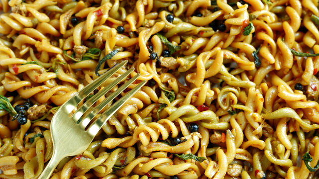 Close-up fork with blurred background of stir-fried pasta with black pepper. Food background of fork and fusili pasta. Spicy food, cooking, healthy, fusion cuisine concept for print, food content, des