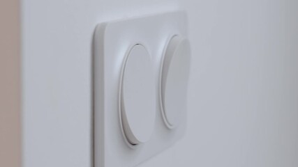 Close-up of hand pressing modern white wall light switch on interior wall to turn on indoor lighting. Concept of electricity use, home control and energy consumption - Powered by Adobe