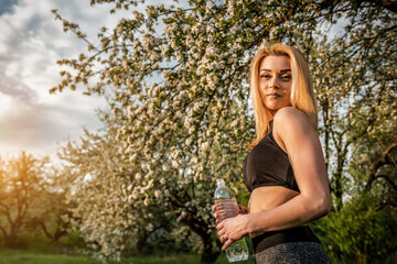 Sporty blonde woman with bottle of water in blooming garden