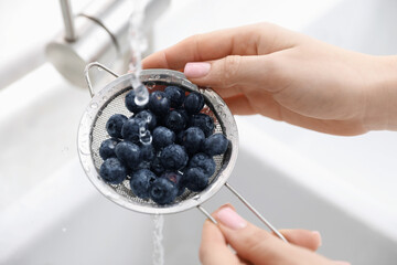 Woman washing blueberries in sieve at sink, closeup
