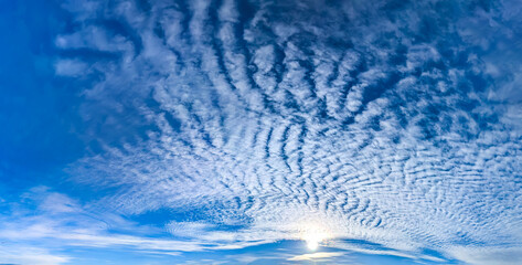 Gorgeous, wide fan of cirrus clouds. Structure feather unfolds panorama. Majestic peacock tail made of cloud with sun at center. Beautiful day with calm blue sky. Background for window website banner.
