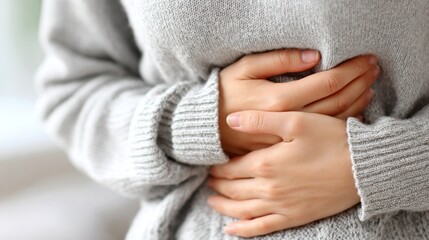 A person cradles their stomach, showing discomfort after eating too much. Dressed in a cozy gray sweater, they reflect on the chaotic aftermath of a delightful meal, seeking solace